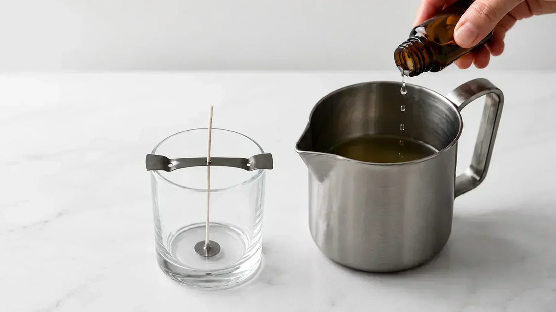 Fragrance oil being added to melted soy wax during handmade candle production with a glass candle jar and centered cotton wick